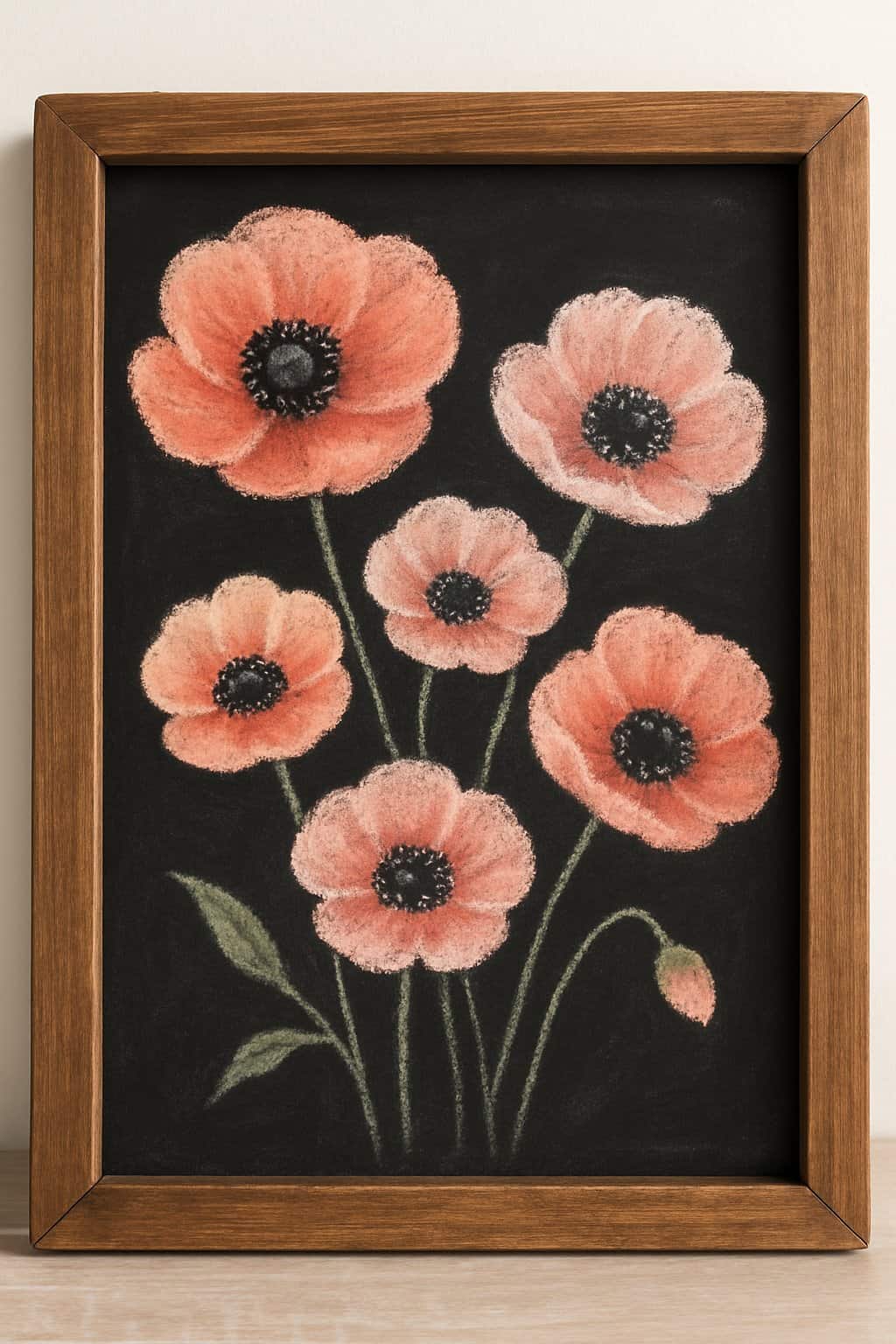 A wood framed chalkboard displaying pastel poppy flowers with black centers on a clean background.
