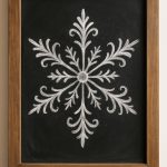 A framed blackboard displays an ornate, symmetrical white chalk drawing of a snowflake with decorative, leafy patterns extending from the center.