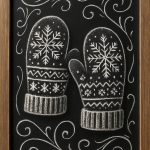 Framed chalkboard drawing of two winter mittens with snowflake and geometric patterns, surrounded by decorative swirls.
