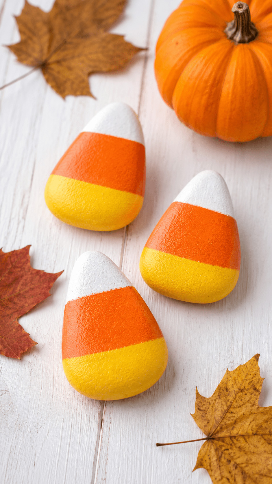 Photo of a painted rock candy corn with gold glitter on orange, yellow, and white bands placed on a wooden mantel.