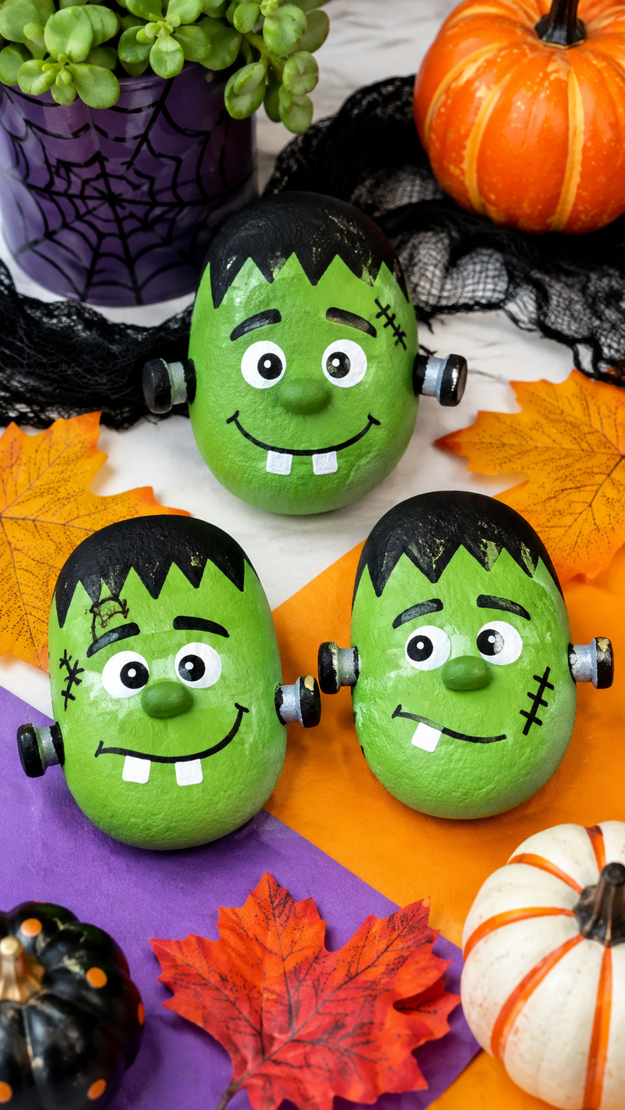 Candy corn Frankenstein painted rock with a lime-green face, black hair, colorful striped body, and mischievous grin on a Halloween display.